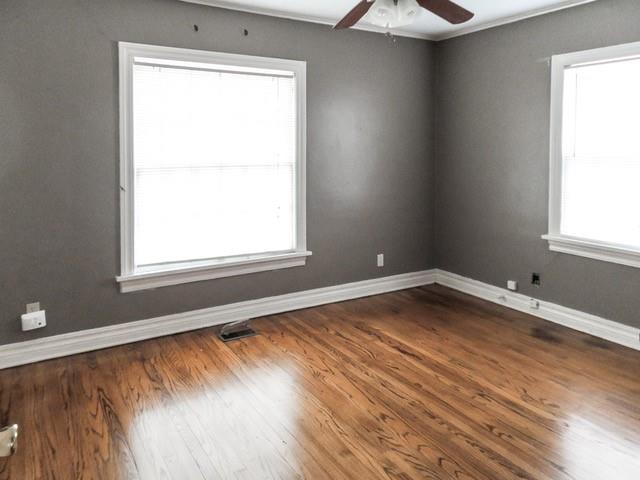 empty room featuring baseboards, a ceiling fan, dark wood-style floors, and visible vents