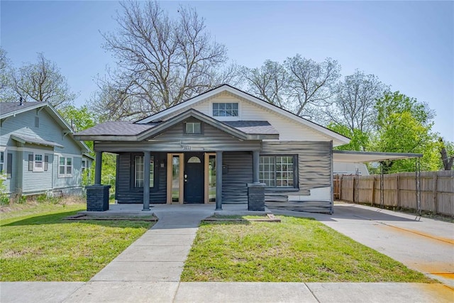 bungalow-style home with fence, a porch, a front yard, concrete driveway, and a carport