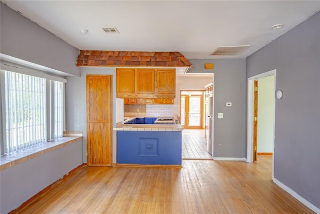 kitchen featuring tile counters, visible vents, tasteful backsplash, and light wood-type flooring