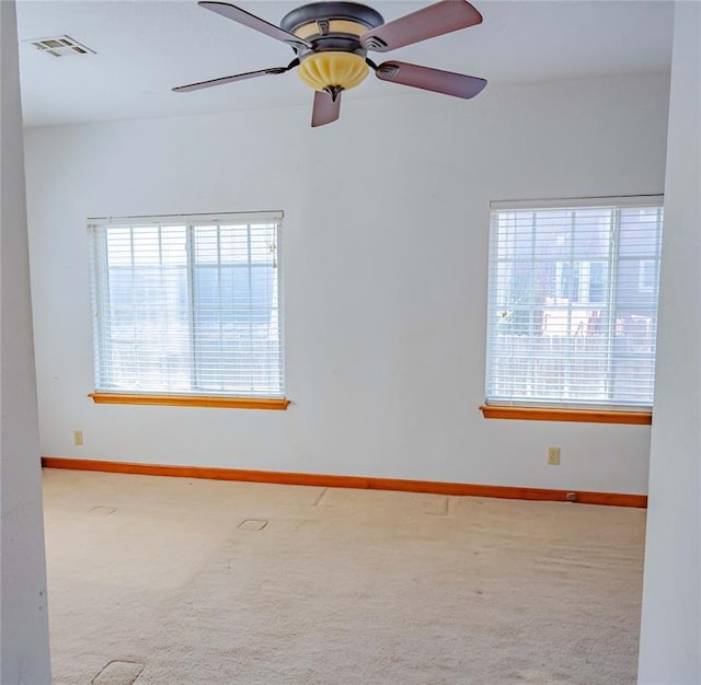 carpeted empty room with visible vents, a ceiling fan, baseboards, and a healthy amount of sunlight