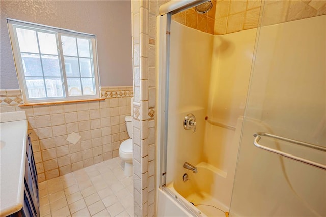 bathroom featuring tile walls, bath / shower combo with glass door, a wainscoted wall, vanity, and toilet