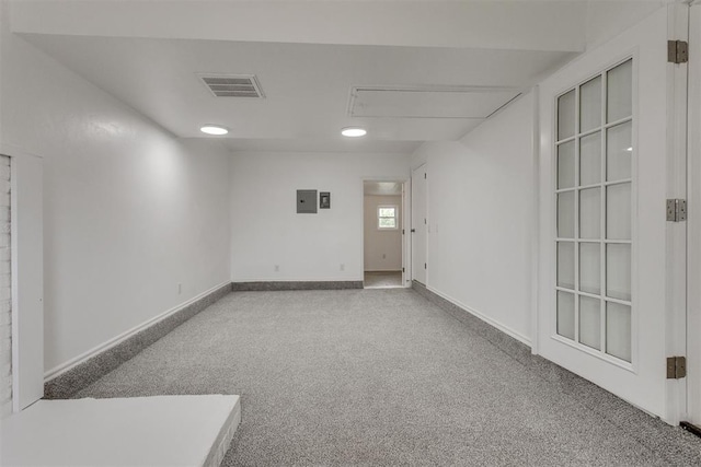 carpeted spare room with visible vents, attic access, baseboards, and electric panel