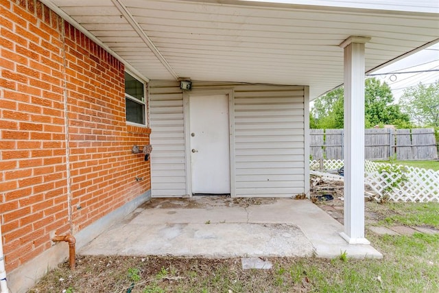 doorway to property featuring brick siding, fence, and a patio