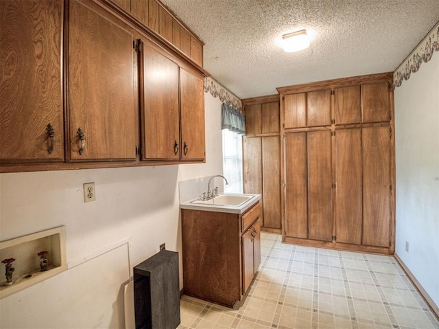 laundry area featuring light floors, a textured ceiling, washer hookup, a sink, and cabinet space