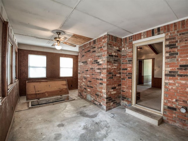unfurnished room with a ceiling fan, unfinished concrete floors, and brick wall