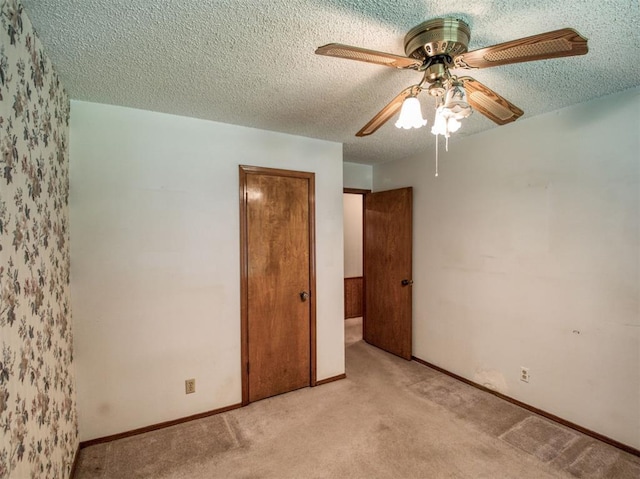 unfurnished bedroom with light colored carpet, a textured ceiling, baseboards, and a ceiling fan