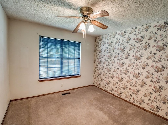 spare room with a textured ceiling, visible vents, ceiling fan, carpet floors, and wallpapered walls
