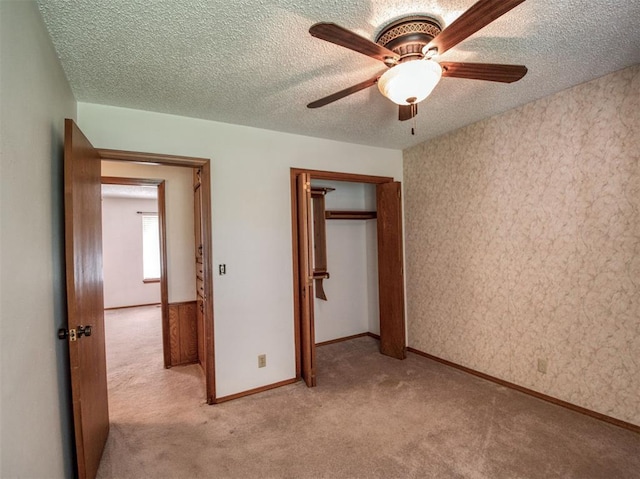 unfurnished bedroom featuring light colored carpet, a textured ceiling, a closet, and baseboards