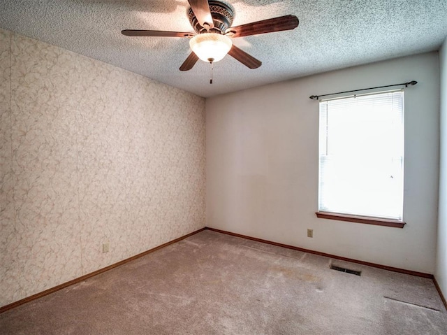 carpeted empty room with a textured ceiling, visible vents, baseboards, and a ceiling fan