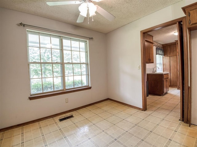 spare room featuring a sink, a textured ceiling, visible vents, baseboards, and ceiling fan