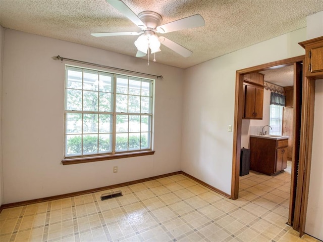 empty room featuring a ceiling fan, a sink, visible vents, and a textured ceiling