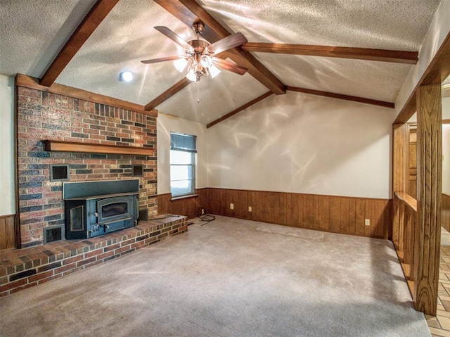 unfurnished living room featuring wood walls, lofted ceiling with beams, a textured ceiling, a ceiling fan, and wainscoting