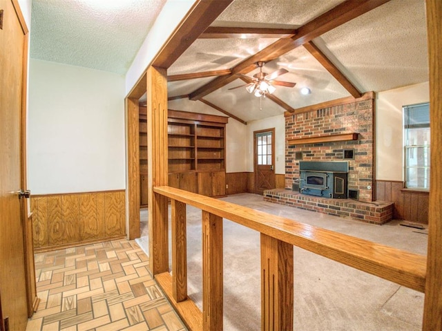 unfurnished living room featuring wainscoting, wooden walls, a textured ceiling, and vaulted ceiling with beams