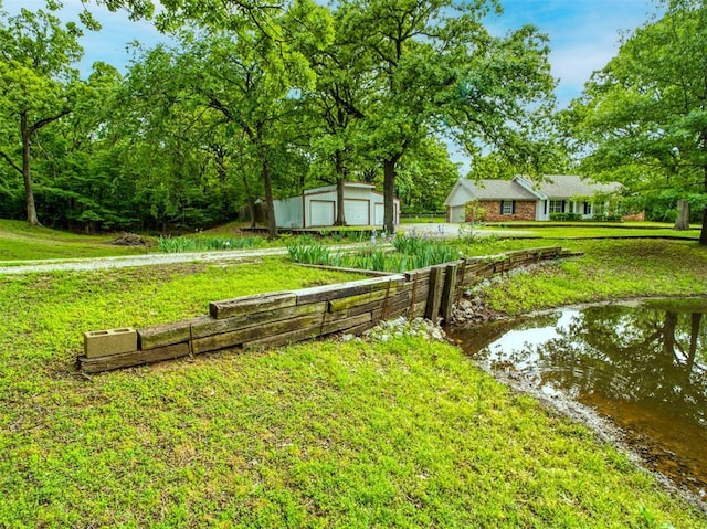 view of yard with a detached garage, a water view, and an outbuilding
