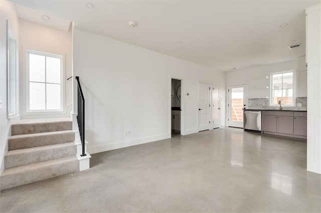 unfurnished living room with visible vents, baseboards, stairway, finished concrete floors, and a sink
