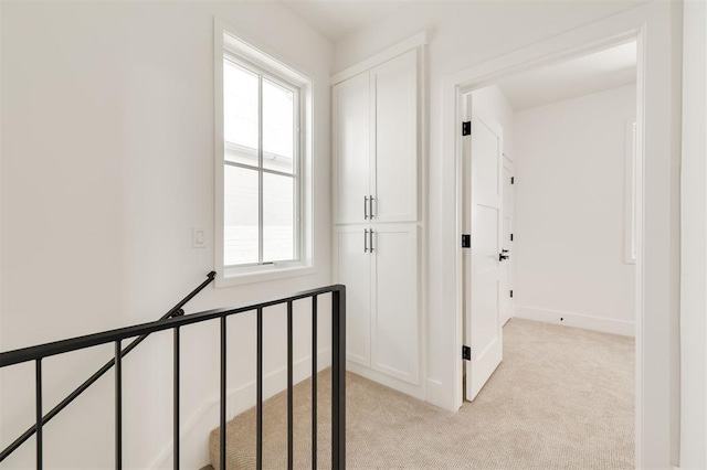 corridor with baseboards, an upstairs landing, and light carpet
