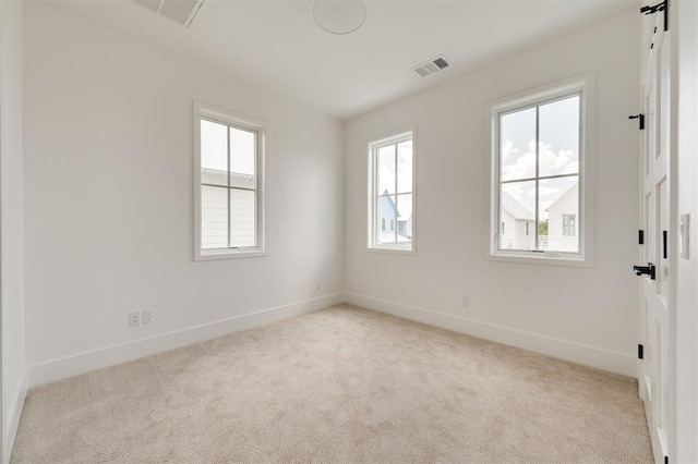 unfurnished room featuring a healthy amount of sunlight, light carpet, and visible vents