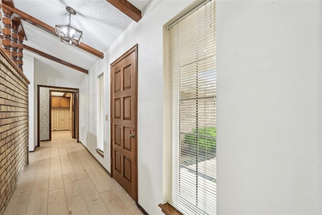 hallway with a textured ceiling, lofted ceiling with beams, and light wood-style floors
