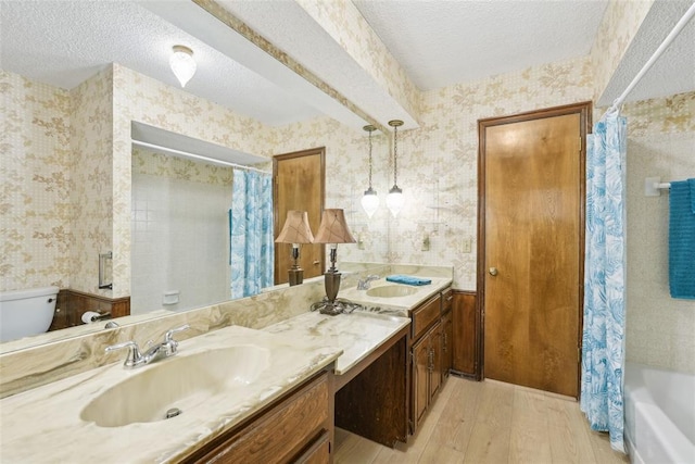 full bathroom featuring a sink, a textured ceiling, wood finished floors, and wallpapered walls