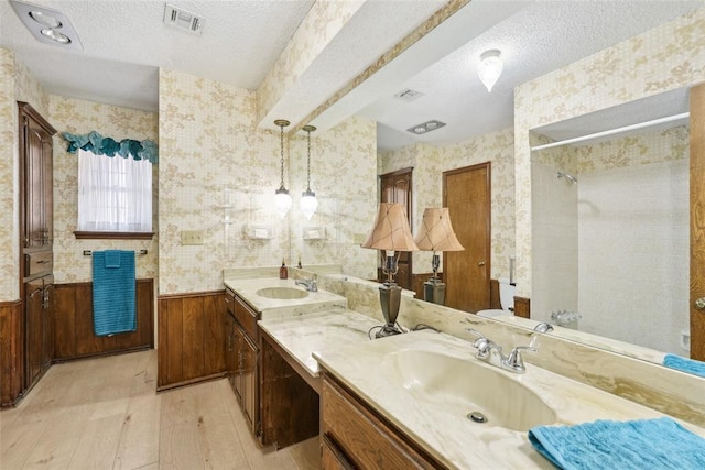 bathroom featuring wood-type flooring, a textured ceiling, a wainscoted wall, and wallpapered walls