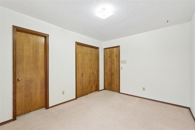unfurnished bedroom featuring baseboards, a closet, a textured ceiling, and light colored carpet