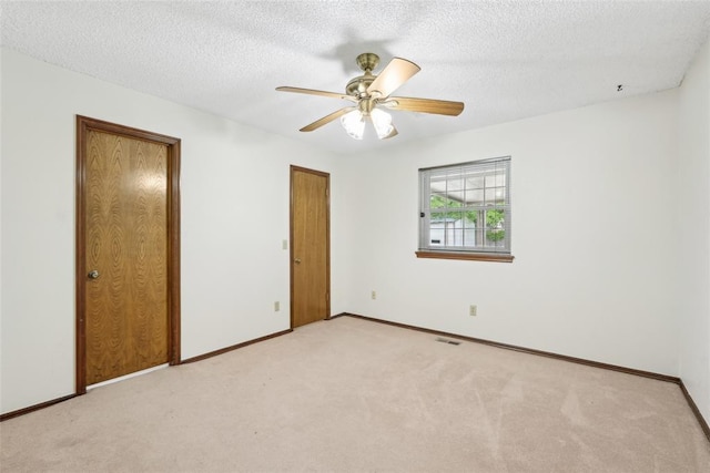 unfurnished bedroom with ceiling fan, light carpet, a textured ceiling, baseboards, and visible vents
