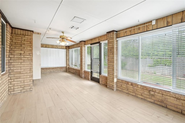 unfurnished sunroom with visible vents, wood finished floors, and brick wall