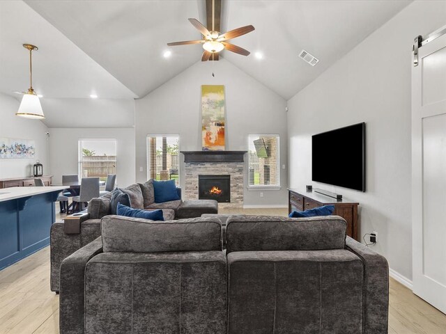 living room with a ceiling fan, high vaulted ceiling, visible vents, a barn door, and a stone fireplace