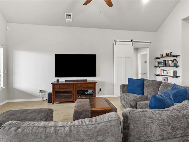 living room with wood finished floors, a barn door, visible vents, ceiling fan, and baseboards