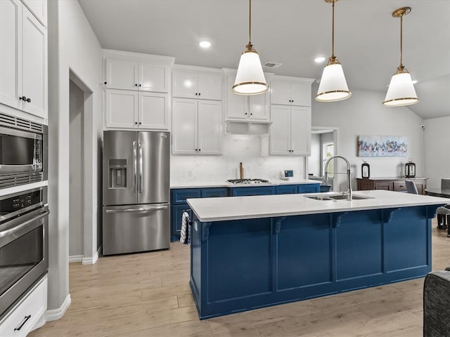 kitchen featuring light wood finished floors, a sink, a kitchen breakfast bar, blue cabinetry, and appliances with stainless steel finishes