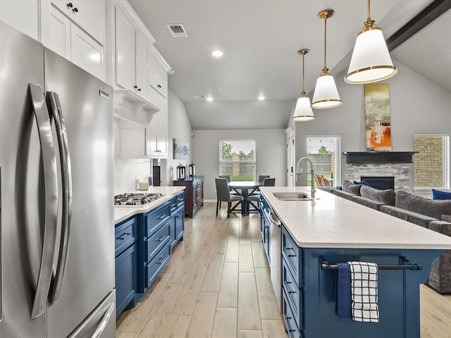 kitchen featuring vaulted ceiling, stainless steel appliances, blue cabinetry, and a sink