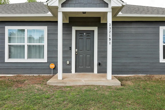 entrance to property featuring a yard and roof with shingles