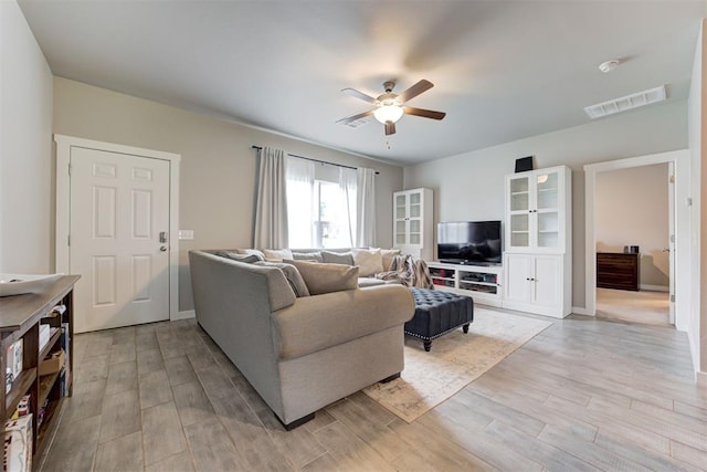 living area featuring visible vents, a ceiling fan, light wood finished floors, and baseboards