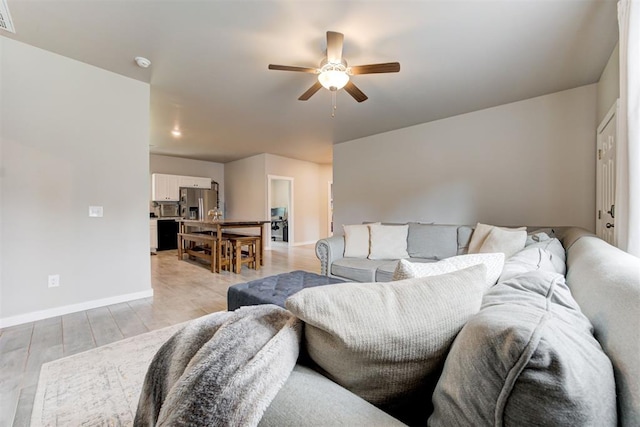 living room with a ceiling fan, baseboards, visible vents, and light wood finished floors