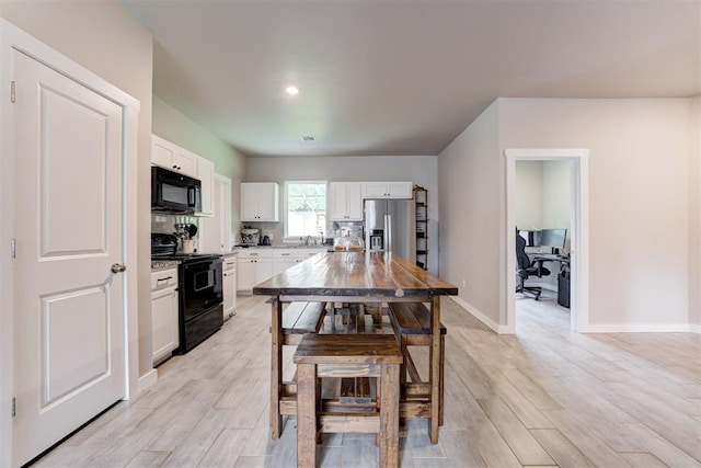 kitchen featuring light wood-type flooring, light countertops, white cabinetry, a sink, and black appliances
