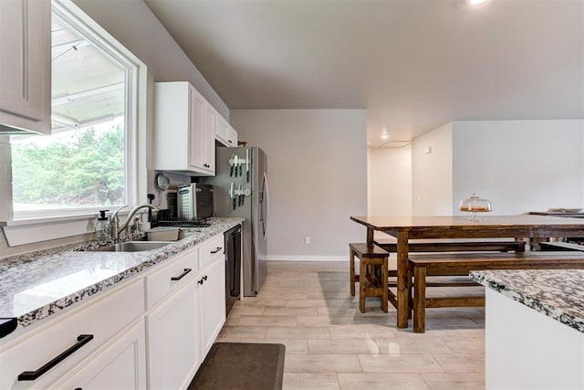 kitchen with white cabinets, light stone countertops, a sink, black dishwasher, and baseboards