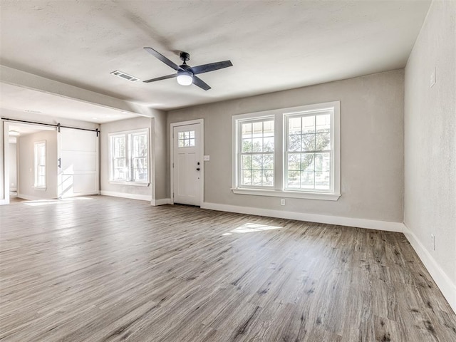 unfurnished living room featuring visible vents, wood finished floors, baseboards, a barn door, and a ceiling fan