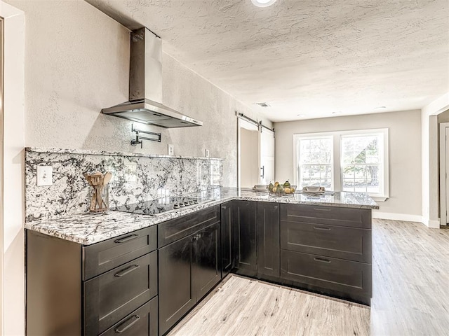 kitchen featuring exhaust hood, light wood-type flooring, black electric cooktop, light stone counters, and a peninsula