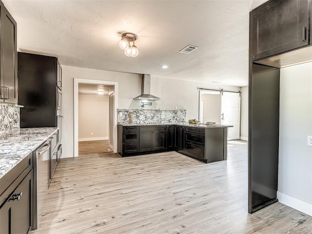 kitchen featuring baseboards, wall chimney exhaust hood, a peninsula, and light stone countertops