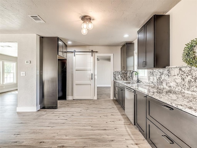 kitchen with a barn door, a sink, light wood-style flooring, stainless steel dishwasher, and visible vents
