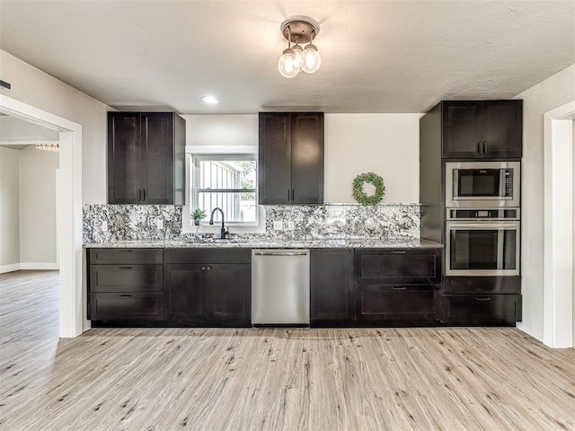 kitchen with light stone counters, appliances with stainless steel finishes, a sink, light wood-style floors, and tasteful backsplash