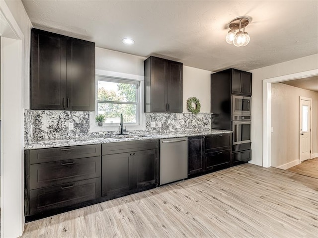 kitchen with light wood-style floors, a sink, appliances with stainless steel finishes, and tasteful backsplash