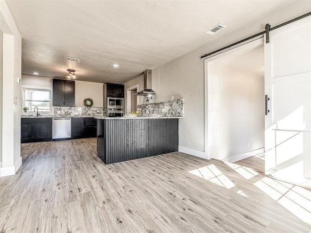 kitchen with visible vents, wall chimney exhaust hood, tasteful backsplash, a sink, and stainless steel appliances