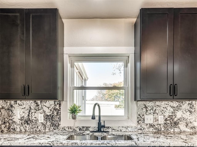 kitchen with a sink, light stone countertops, and backsplash