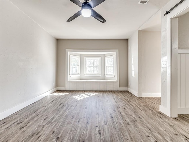 unfurnished living room with baseboards, a barn door, ceiling fan, and wood finished floors