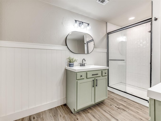 full bathroom featuring visible vents, vanity, wood finished floors, a wainscoted wall, and a tile shower