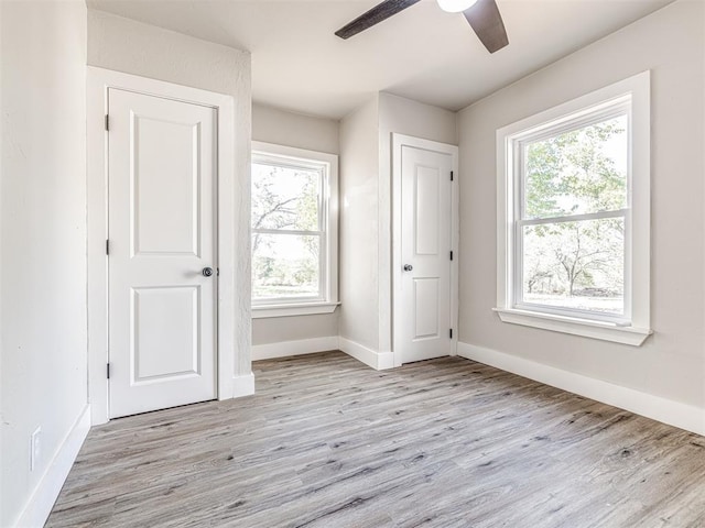 unfurnished bedroom featuring light wood-style floors, baseboards, multiple windows, and ceiling fan