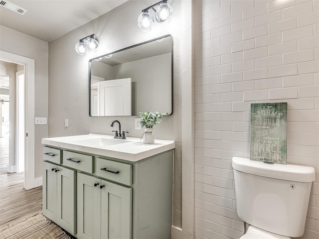 bathroom with vanity, toilet, wood finished floors, and visible vents