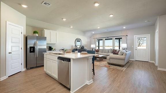 10232 NW 28th St, Yukon, OK 73099 - kitchen with white cabinets, appliances with stainless steel finishes, an island with sink, and light wood-style floors