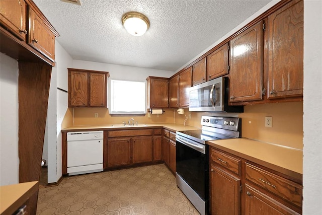 208 Harrogate Dr, Yukon, OK 73099 - kitchen with appliances with stainless steel finishes, a sink, a textured ceiling, light floors, and light countertops